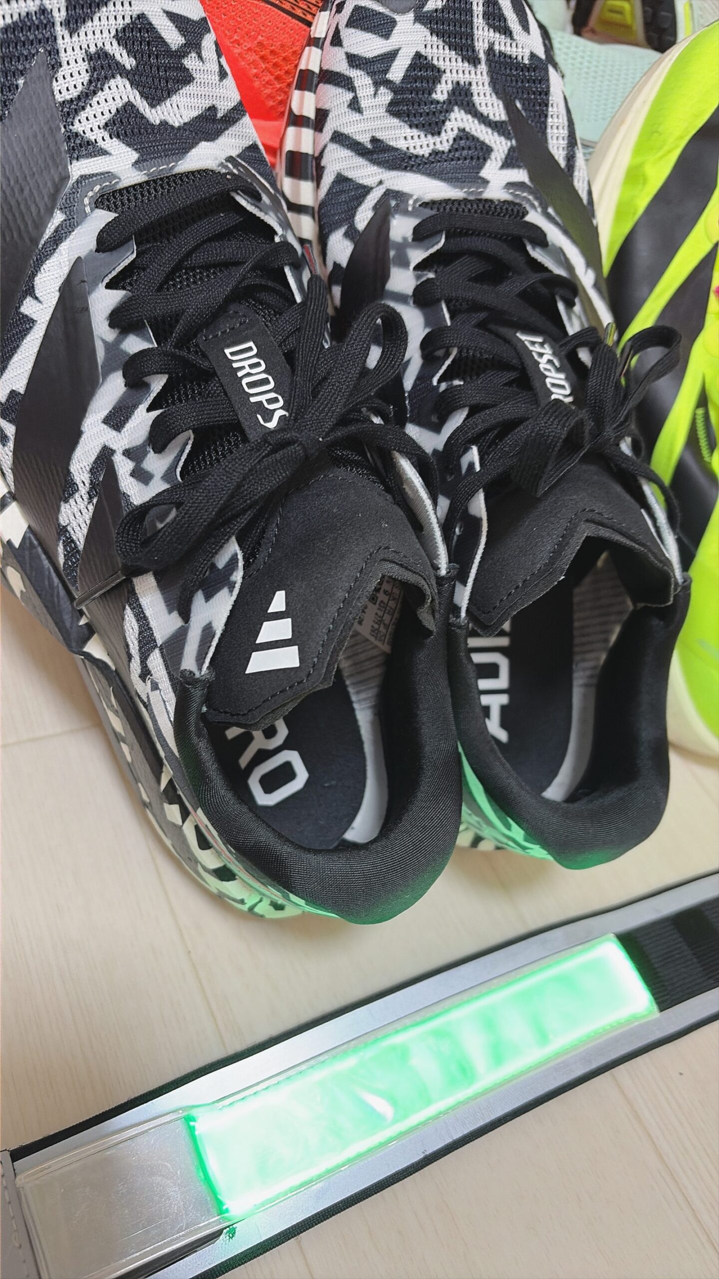 アディダス アディゼロ ドロップセット。白黒の柄で、ベロに DROPSET の文字。手前に緑に光るラインライト
