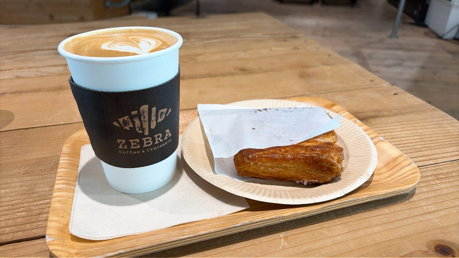 ZEBRA Coffee & Croissant の紙コップに入ったラテと、木の皿にのったクロワッサン