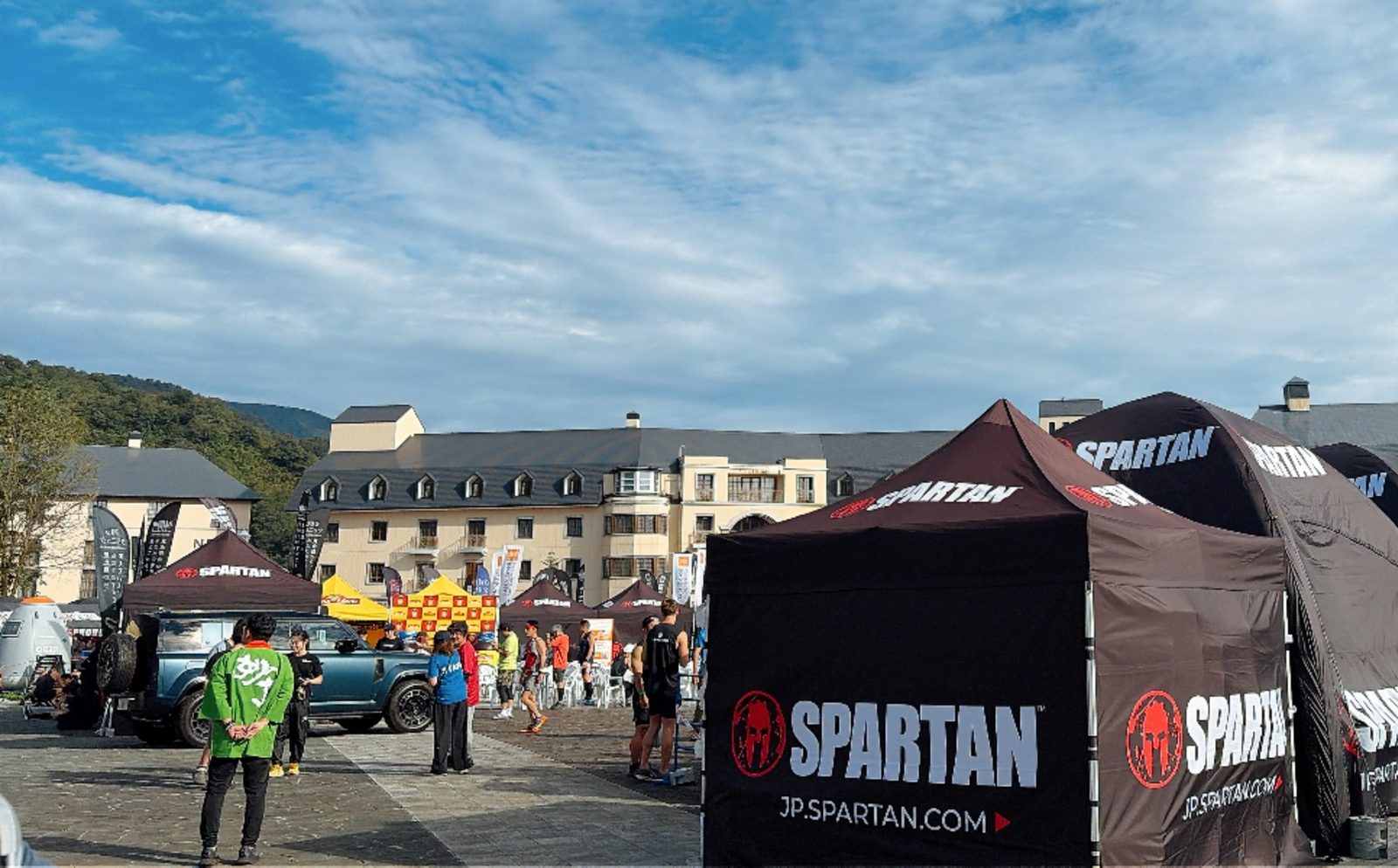 スパルタンレースの会場。青空の下、SPARTAN の黒いテントが並び、奥にホテルの建物