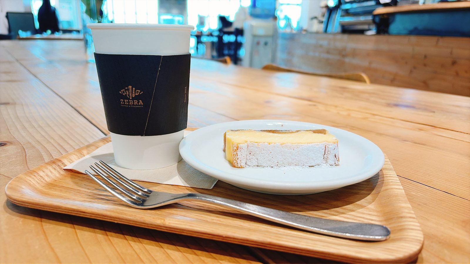 ZEBRA Coffee & Croissant のコーヒーと、りんごがのったチーズケーキ。木のトレイにフォークとナイフ