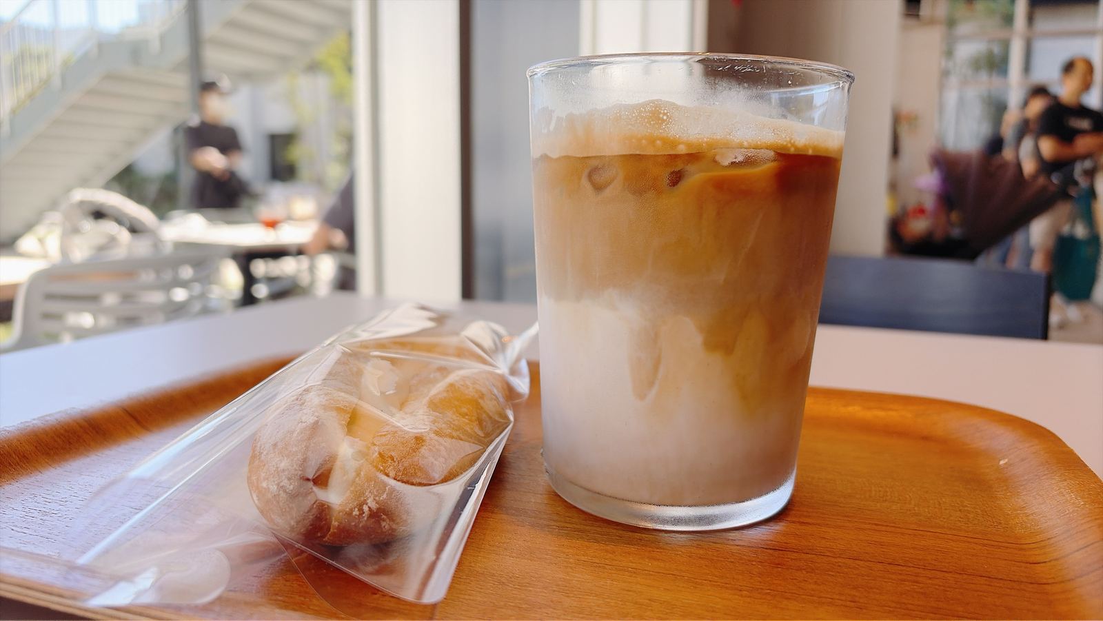 カフェのテーブル。木のトレイにのったアイスラテと、袋に入ったパン