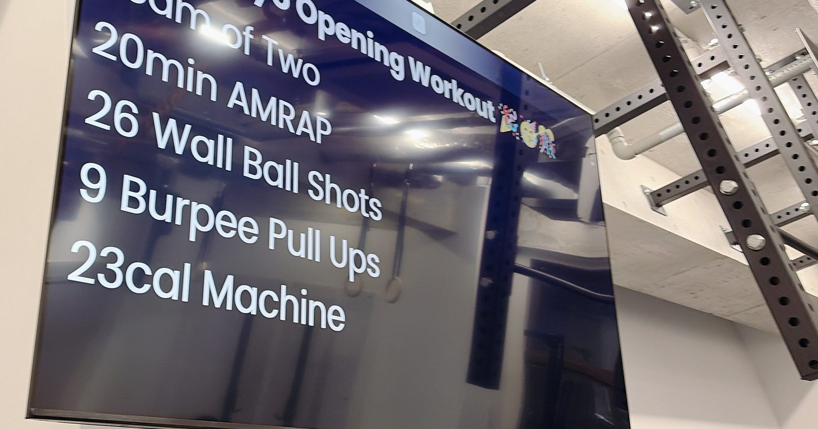 ジムのモニターに映ったオープニングのメニュー。Team of Two、20min AMRAP、26 Wall Ball Shots、9 Burpee Pull Ups、23cal Machine