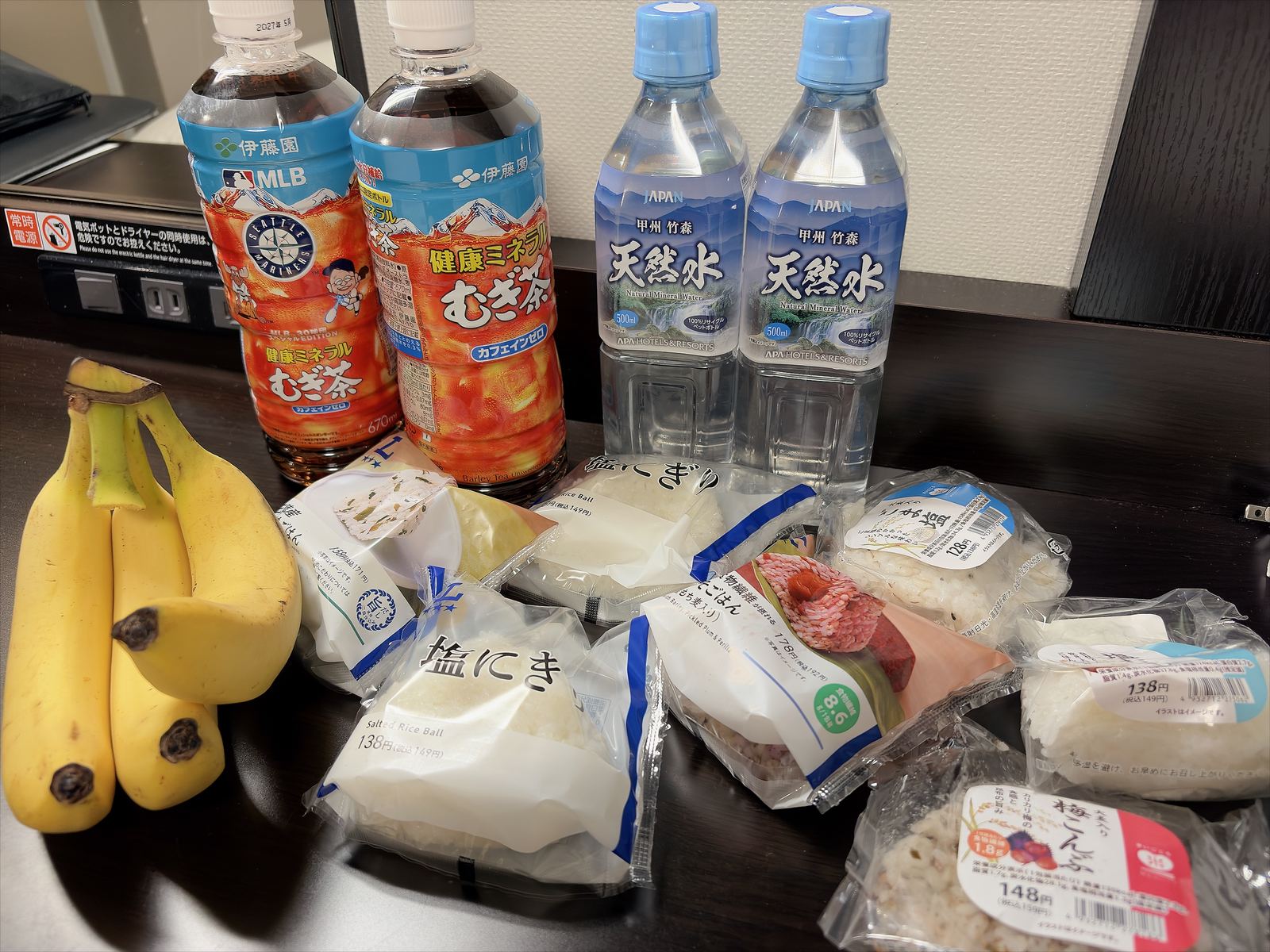 ホテルの机に並べた、おにぎりとバナナ、むぎ茶と水のペットボトル